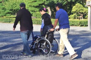 一般的な車いすを3名で介助して進むようす