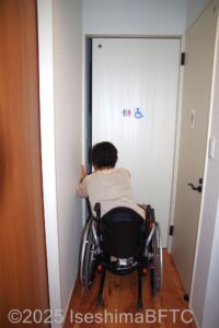 車いす対応トイレの入口を開けようとしている車いすの女性