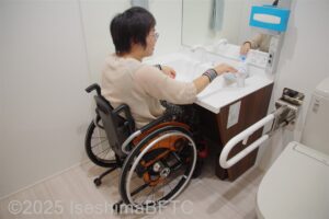 車いす対応の洗面台で水を出す車いすの女性