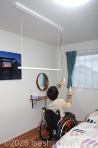 室内物干しを操作棒で下ろす車いすの女性