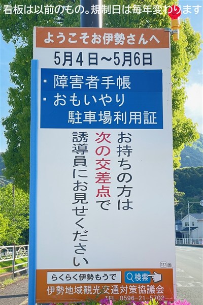 「障害者手帳とおもいやり駐車場利用証をお持ちの方は次の交差点で誘導員にお見せください」と書いてある立て看板