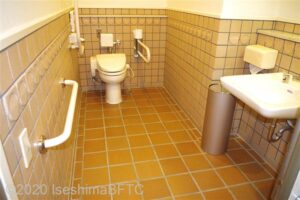 車いす対応トイレの個室内のようす。便器に向かって左側奥の壁にはL字手すり、右側にはU字の可動式手すりが付いている。車いすトイレにしては幅が125㎝と狭い。