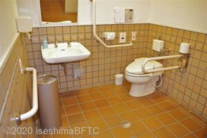 車いす対応トイレの個室内のようす。便器に向かって左側奥の壁にはL字手すり、右側にはU字の可動式手すりが付いている。