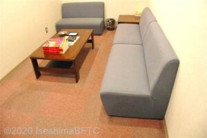 カラオケハウスの室内のようす。細長い部屋。グレーのソファーが置かれて切る。