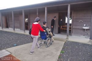 海女小屋の入口へ入ろうとする男女。男性は車いすに乗って、女性がその車いす押しているようす。