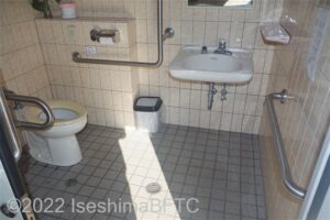 アメニティ道路磯辺ステーション車いす対応トイレ　入口からみて左奥に、よこ置きに便器。入口からみて右奥に洗面台
