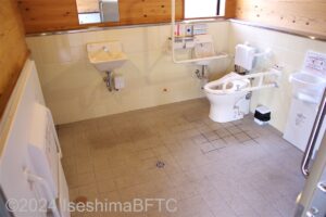 的矢あんしんトイレ　車いす対応トイレ大　入口からみて右奥に、よこ置きに便器。入口正面に洗面台、左にユニバーサルシート、右にオストメイト