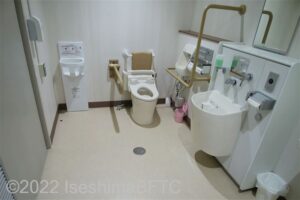 阿児アリーナ　オーシャンホール車いす対応トイレ　入口からみて左奥に、よこ置きに便器。入口からみて正面に洗面台