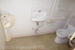 賢島駅南口駐車場車いす対応トイレ室内　入口からみて右に、よこ置きに便器。入口正面に洗面台