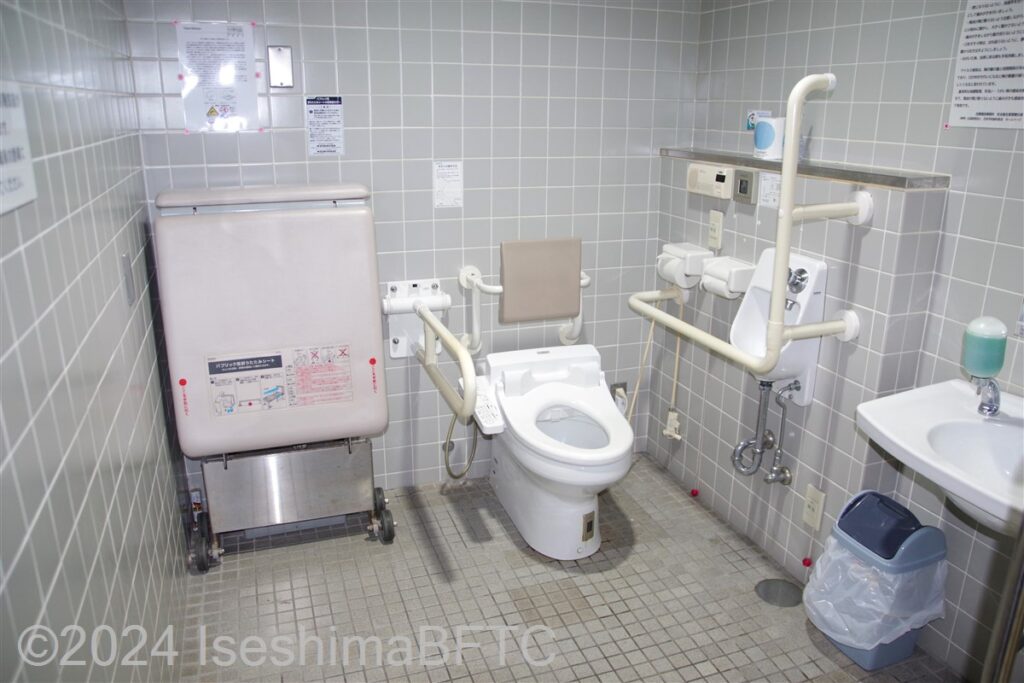 志摩庁舎1階車いす対応トイレ内部全景　入口からみて右奥に、よこ置きに便器。入口からみて右手前に洗面台