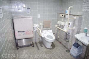 志摩庁舎1階車いす対応トイレ内部全景　入口からみて右奥に、よこ置きに便器。入口からみて右手前に洗面台