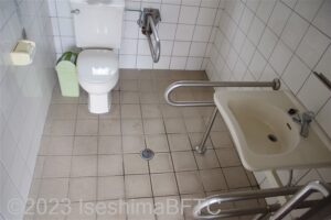 黒崎小公園車いす対応トイレ内部　入口正面奥に、たて置きに便器。入口からみて右手前に洗面台