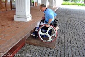 ホテルの玄関ポーチには10㎝の段差があるので、簡易スロープの準備あり。写真は車いすの男性が簡易スロープを上がっているようす。