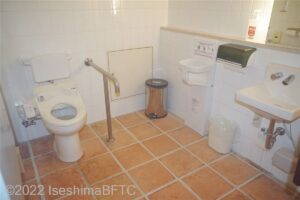 車いす対応トイレの個室内のようす。便器に向かって左側奥の壁にはL字手すり、右側にはI字手すりが付いている。