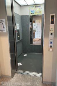 エレベーターの中のようす。手すりや後方確認のための鏡、低い位置の操作盤が付いている。