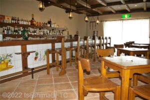 スペイン風居酒屋「カルメン」の室内のようす。木のイスとテーブルが置かれている。バーカウンターの全面には、スペイン風の絵が描かれたタイルが貼られている。