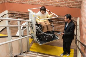 スタッフの操作で2階段昇降機で踊り場を通過する車いす使用者