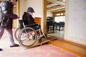 宴会場入口の段差を簡易スロープで上がる車いす使用者