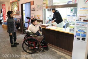 受付のカウンター越しにスタッフと話しをする車いすの女性のようす