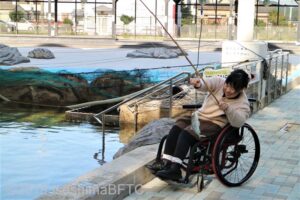 車いすの女性がアジを釣り上げているようす。