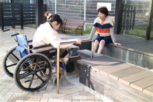足湯体験をしている女性2名。一人は車いすに乗っていて、バリアフリーに配慮された造りの足湯に漬かっている。
