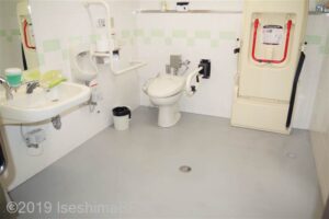 車いす対応トイレの室内のようす。
便器の左側の壁にはL字手すり、右側には可動式のU字手すりが設置されている。便器の右側にはユニバーサルシートあり。